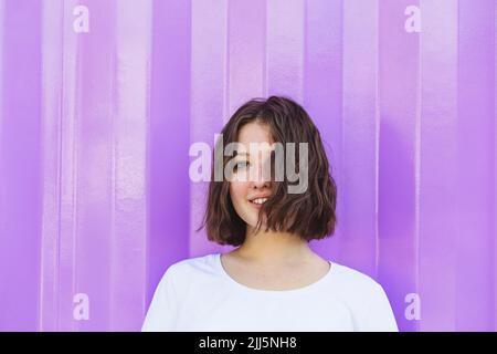 Lächelndes Teenager-Mädchen mit braunen Haaren vor dem lila Frachtcontainer Stockfoto