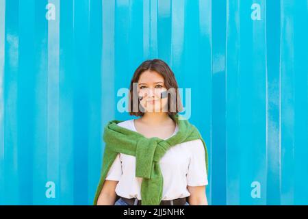 Lächelndes Teenager-Mädchen mit Friedenssymbol und EU-Farbe auf den Wangen, die vor dem blauen Frachtcontainer stehen Stockfoto