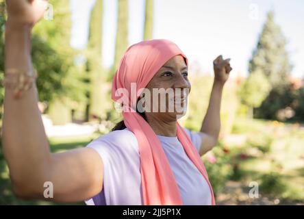 Fröhliche ältere Frau mit Training im Park mit gebeugten Muskeln Stockfoto