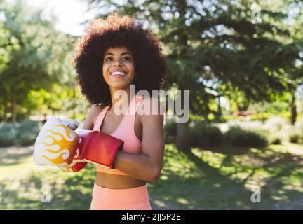 Glückliche Frau mit Boxhandschuhen im öffentlichen Park Stockfoto