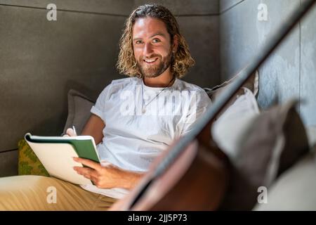 Lächelnder Komponist mit Buch und Gitarre zu Hause Stockfoto