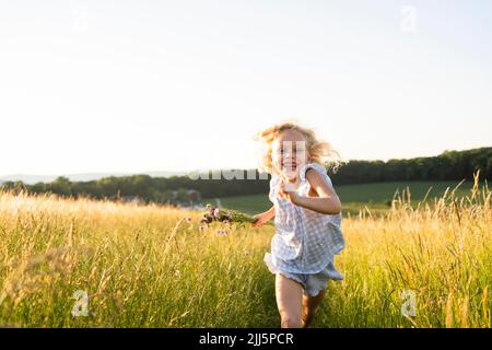 Fröhliches Mädchen, das am sonnigen Tag im Feld läuft Stockfoto