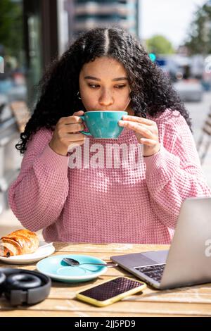 Junge Frau, die Kaffee trinkt, sitzt im Straßencafé Stockfoto