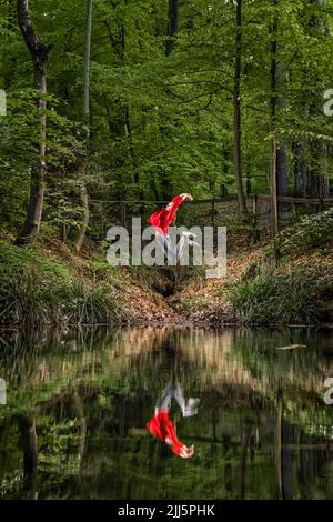 Frau mit erhobenen Armen, die durch Spiegelung im See springen Stockfoto