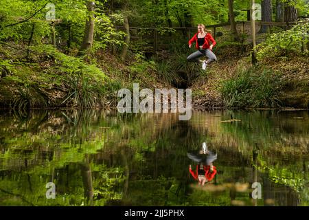 Frau, die im Wald über den See springt Stockfoto