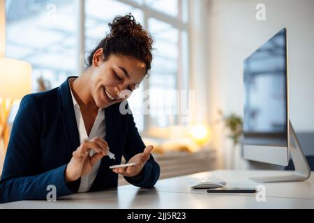 Glückliche Geschäftsfrau, die am Schreibtisch im Büro einen Schwangerschaftstest macht Stockfoto