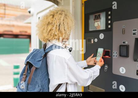 Frau, die den Ticketautomaten benutzt, scannt den QR-Code über das Smartphone Stockfoto