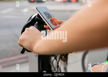 Frau scannt Barcode über Smartphone und mietet ein Elektrofahrrad Stockfoto