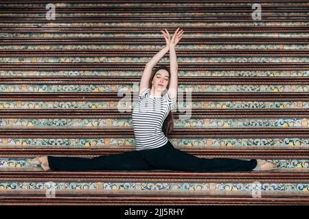 Balletttänzerin mit erhobenen Armen übt Splits auf der Treppe Stockfoto