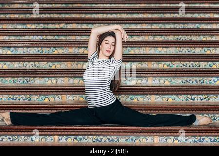 Frau mit erhobenen Armen, die Splits auf der Treppe macht Stockfoto