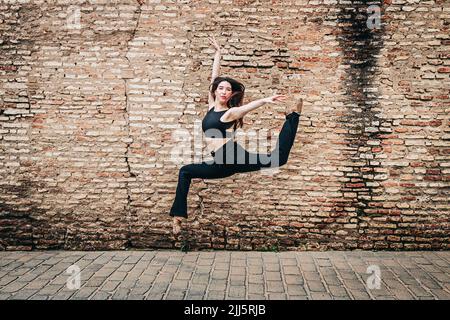 Junge Balletttänzerin, die vor einer Backsteinmauer tanzt Stockfoto