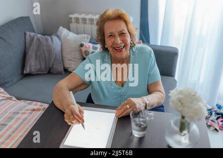 Glückliche ältere Frau mit Tablet-PC am Tisch Stockfoto