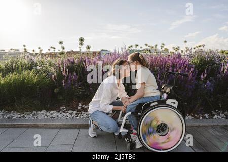 Tochter im Rollstuhl küsst Mutter im Park Stockfoto