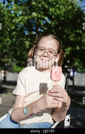 Lächelndes Mädchen, das mit Eis im Rollstuhl im Park sitzt Stockfoto