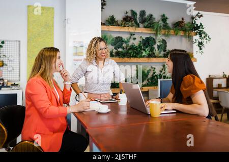 Glückliche, multirassische Kollegen aus der Wirtschaft diskutieren am Schreibtisch im Büro Stockfoto