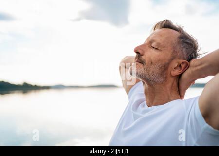 Reifer Mann, der sich mit geschlossenen Augen am See entspannt Stockfoto