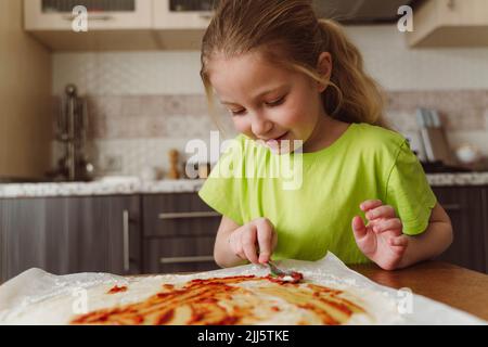 Mädchen verteilen Tomatensauce auf Pizzateig Stockfoto