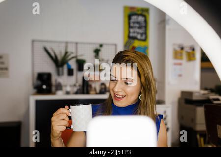 Junge Geschäftsfrau mit Becher vlogging im Büro Stockfoto