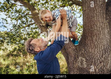 Glücklicher Vater spielt mit Sohn an Baum Stockfoto