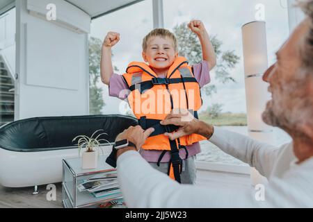 Glücklicher Sohn trägt Rettungsweste, die Muskeln zu Hause anbiegt Stockfoto