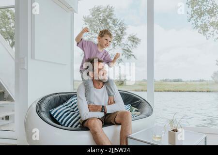 Glücklicher Sohn, der Spaß mit dem Vater hat, der zu Hause auf dem Sofa sitzt Stockfoto