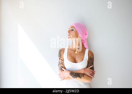 Frau mit Kopftuch, die mit gekreuzten Armen vor der Wand steht Stockfoto