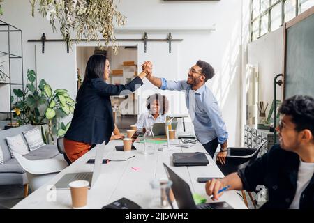 Ein glücklicher Geschäftsmann und eine Geschäftsfrau, die im Büro fünf Punkte über den Schreibtisch verteilt hat Stockfoto