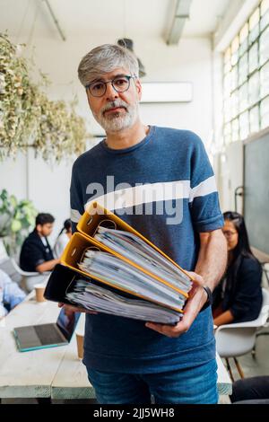 Reifer Geschäftsmann mit Brillen, die Akten am Arbeitsplatz halten Stockfoto