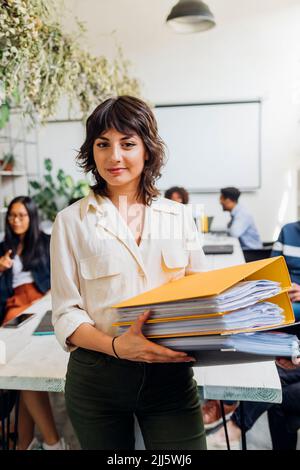 Selbstbewusste Geschäftsfrau, die im Coworking Office Akten hält Stockfoto