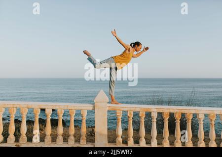 Frau balanciert auf dem Geländer am Meer Stockfoto