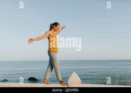 Frau balanciert am sonnigen Tag auf dem Geländer am Meer Stockfoto