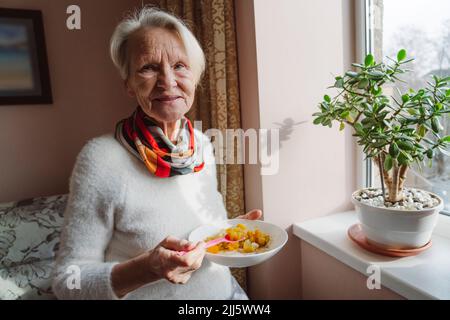 Glückliche ältere Frau mit Schale am Fenster Stockfoto