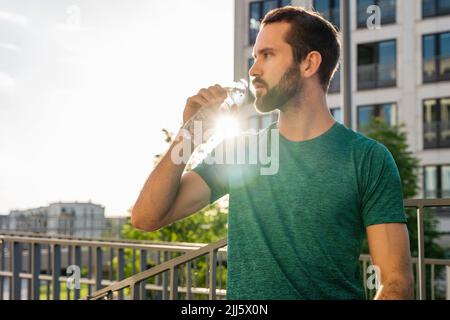 Junger Mann, der an einem sonnigen Tag Wasser trinkt Stockfoto