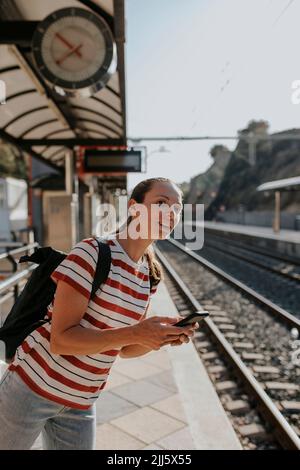 Lächelnde Frau mit Telefon am Bahnsteig Stockfoto