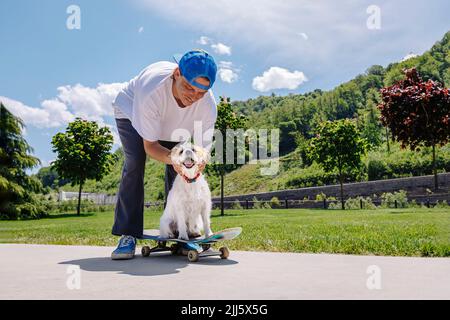 Lächelnder Mann streichelte Hund auf dem Skateboard Stockfoto
