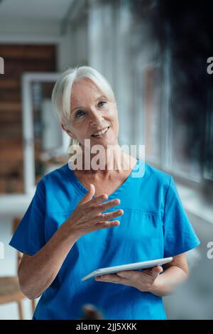 Lächelnde Krankenschwester, die den Tablet-PC gestikuliert hält Stockfoto
