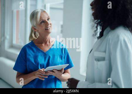 Lächelnde Krankenschwester mit Tablet-PC im Gespräch mit Ärztin Stockfoto