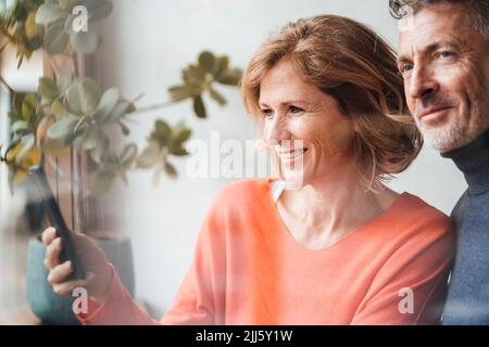 Lächelnder Mann, der bei einer Frau mit einem Smartphone im Café steht Stockfoto