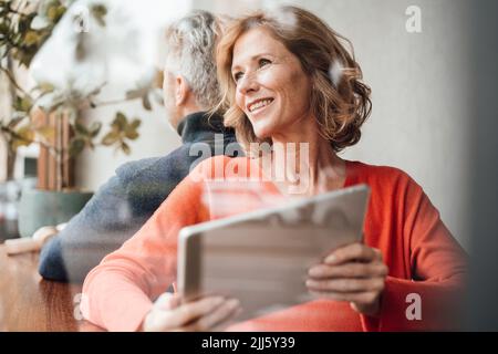 Lächelnde Frau mit Tablet-PC vor dem Mann im Café Stockfoto