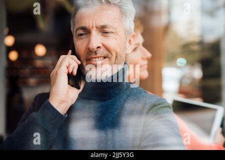 Mann, der auf dem Mobiltelefon spricht und vor einer Frau sitzt, die einen Tablet-PC im Café hält Stockfoto