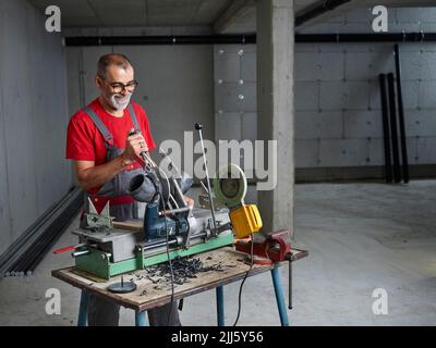 Lächelnder Klempner mit Brillen, der Kunststoffrohr an der Werkbank schneidet Stockfoto