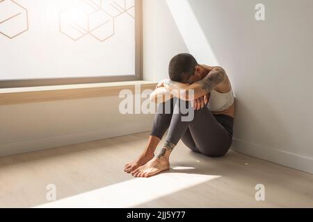 Traurige Frau, die am Fenster am Boden saß Stockfoto