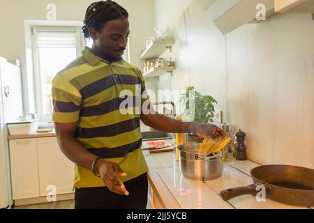 Junger Mann, der ungekochte Spaghetti in den Kochtopf in der Küche legt Stockfoto