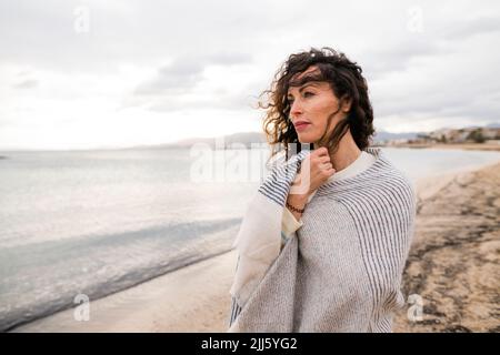 Nachdenkliche Frau in Schal am Strand gewickelt Stockfoto