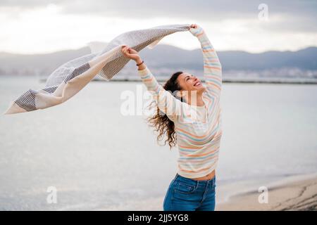 Glückliche Frau mit erhobenen Armen hält Schal Stockfoto