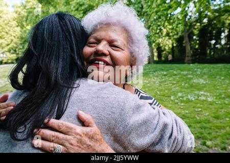 Lächelnde Mutter umarmt Tochter im Park Stockfoto