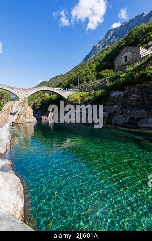 Schweiz, Tessin, Lavertezzo, klare Oberfläche des Verzasca Flusses mit Ponte dei Salti Bogenbrücke im Hintergrund Stockfoto