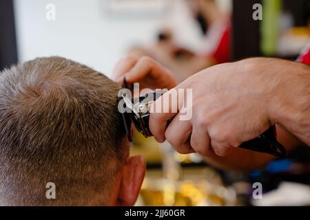 Ein alter Mann, der in einem Friseurladen einen Haarschnitt von einem Meister genießt. Ein alter Mann bekommt einen stylischen Haarschnitt Stockfoto