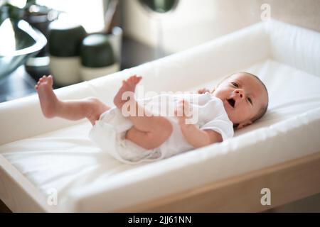 Aufgewütteltes Baby, das Arme und Beine winkt, während es auf dem Windelwechsler liegt Stockfoto