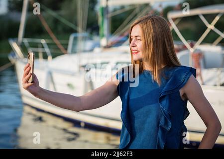 Frau, die Selfie-Fotos auf dem Smartphone gemacht hat, während sie auf dem Jachthafen steht Stockfoto